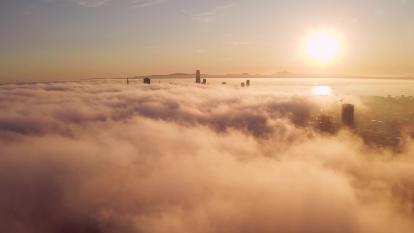 Flying over the clouds during morning sunrise in San Francisco with skyscrapers rising above the clouds. Beautiful Californian morning in San Francisco.