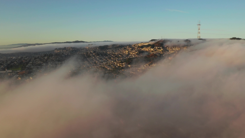 Flying over the clouds during morning sunrise in San Francisco with skyscrapers rising above the clouds. Beautiful Californian morning in San Francisco.