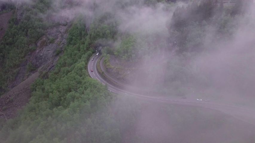 Drone footage of cars driving on a mystic and foggy mountain road in Norway.