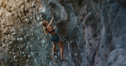 Young fit woman lead rock climbing on sport route, outdoors rock climbing, cinematic slow motion rock climbing moments