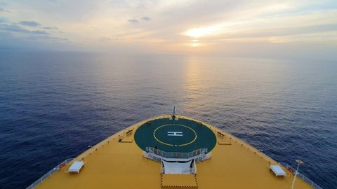 Bow of cruise ship moving over water toward sunrise
