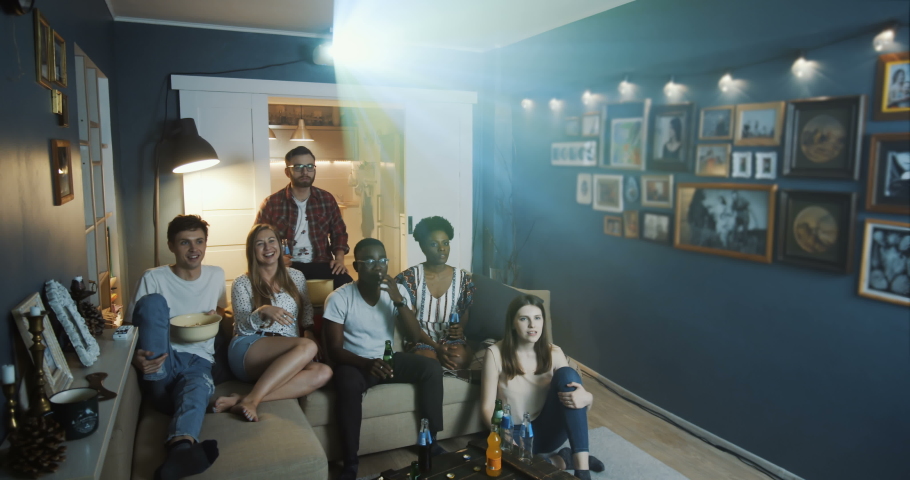 Happy young multiethnic company of friends watching football on TV at home using projector, smile and cheer slow motion. | Shutterstock HD Video #1037385656