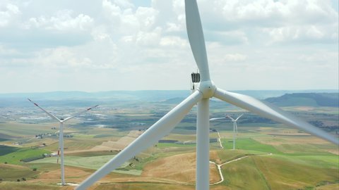 Aerial close-up shot of rotating wind turbines generating green energy in beautiful landscape of Basilicata in Southern Italy