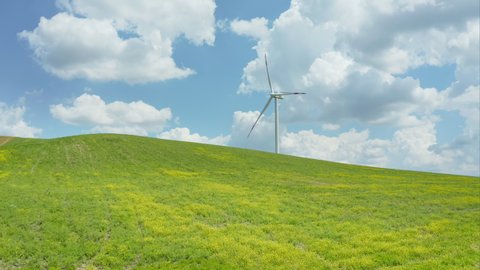 Aerial shot of wind turbine generating clean energy with green field on foreground and blue sky with clouds on background, in a beautiful calm and pieceful countryside of Basilicata in Southern Italy