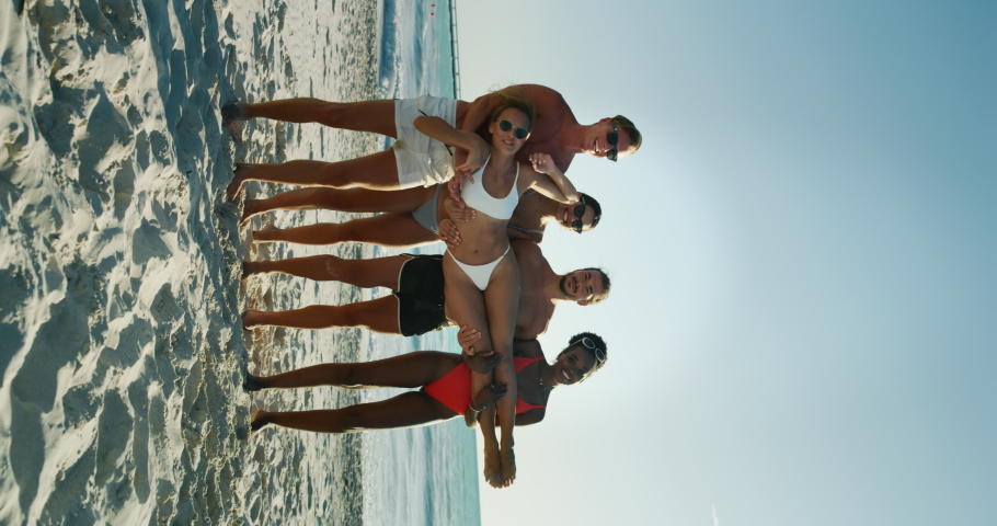 Vertical shot of young multi-ethnic friends in swimwear are having fun to enjoy their summer vacation together on a beach with a sea in a sunny day.