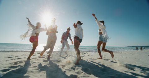 Slow motion of young multi-ethnic friends  are having fun to enjoy their summer vacation together on a beach with a sea in a sunny day.
