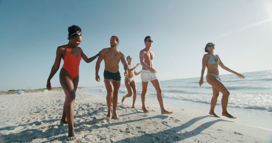 Slow motion of young multi-ethnic friends in swimsuits are walking on a beach enjoying their summer vacation together on a beach with a sea in a sunny day. Royalty-Free Stock Footage #1037399585