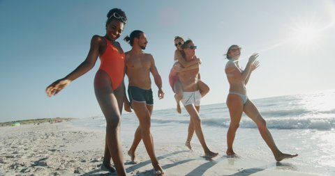 Slow motion of young multi-ethnic friends in swimsuits are walking on a beach enjoying their summer vacation together on a beach with a sea in a sunny day.