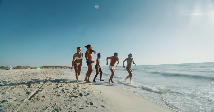 Slow motion of young multi-ethnic friends in swimsuits are walking on a beach enjoying their summer vacation together on a beach with a sea in a sunny day. Royalty-Free Stock Footage #1037399588