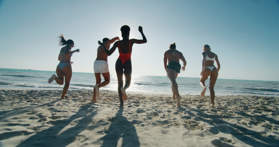 Slow motion of young multi-ethnic carefree  friends in swimsuits are having fun with a water and enjoying their summer vacation together on a beach with a sea in a sunny day. Royalty-Free Stock Footage #1037399801