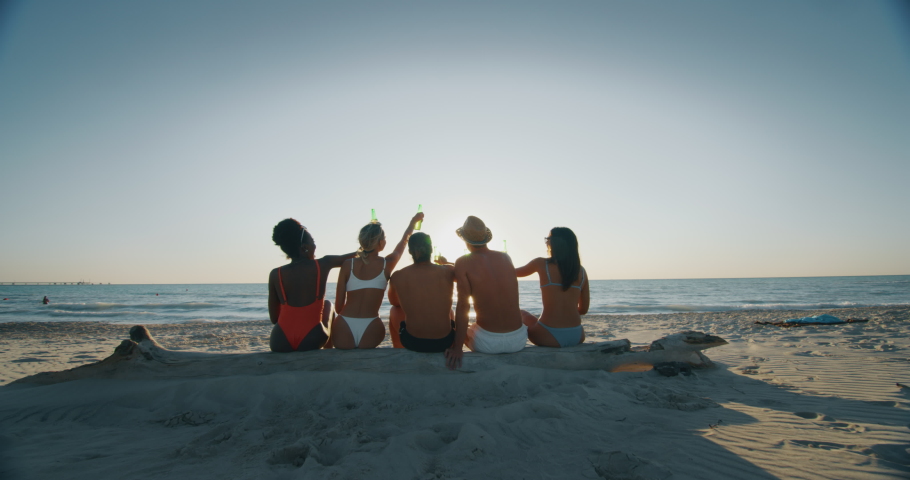 Slow motion close up of young multi-ethnic friends in swimwear are cheering with a beer for a start of their summer vacation together on a beach with a sea on a sunset. Royalty-Free Stock Footage #1037401001
