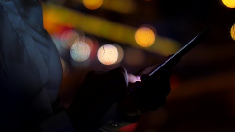 Business woman texting or using smartphone, closeup shot of device in hands. Dark room at late hour, blurred city lights seen on background, cars traffic on road
