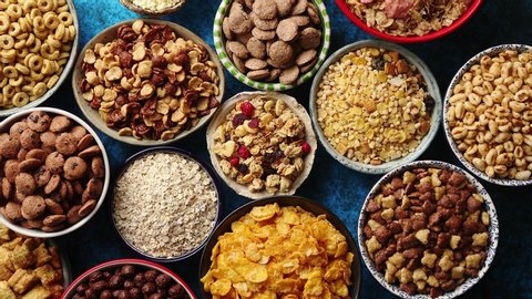 Assortment of various kinds cereals placed in ceramic bowls with cornflakes, granola, cereals and oatmeal. Flat lay, top view on blue rusty table with copy space in the middle