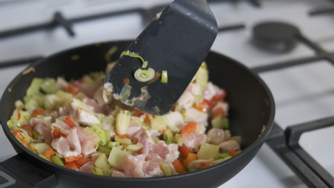 Meat with vegetables on the stove. A woman`n hand with a spatula mixes a fried vegetables in the fry pan. Meat, pepper, lettuce are in the pan.