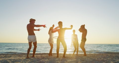 Slow motion of young multi-ethnic carefree  friends in swimsuits are having fun and enjoying their summer vacation together on a beach with a sea on a sunset.