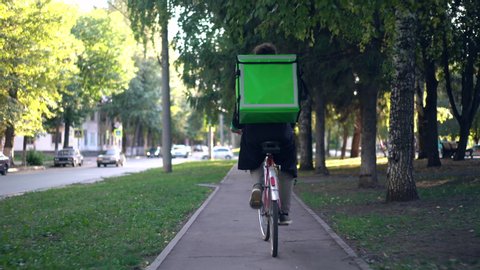 delivery man with green backpack rides a bicycle through the city with food delivery.