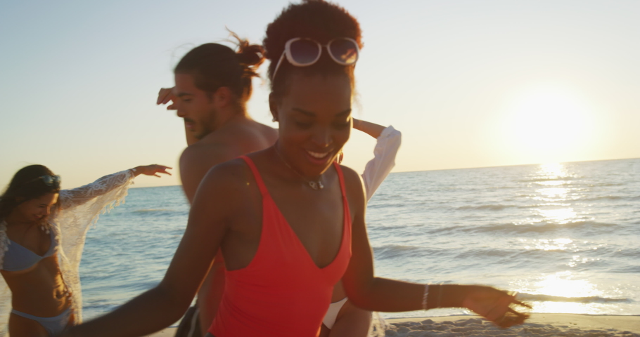 Slow motion close up of young multi-ethnic carefree  friends in swimsuits are having fun and enjoying their summer vacation together on a beach with a sea on a sunset. Royalty-Free Stock Footage #1037413415