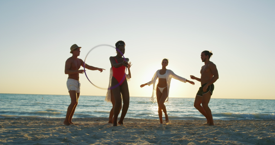 Slow motion of young multi-ethnic carefree  friends in swimsuits are having fun and enjoying their summer vacation together on a beach with a sea on a sunset. Royalty-Free Stock Footage #1037413439
