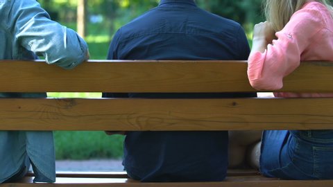 Woman hugging one man holding hand of another, sitting on bench, betrayal