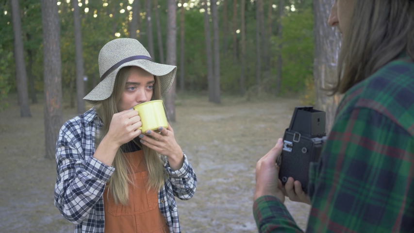 Young pretty caucasian woman posing with a yellow cup on the background of forest. Boyfriend taking pictures of his lovely girl on vacations