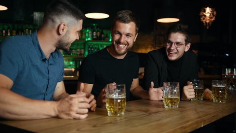 Male friends resting in the pub with beer in hands and talking.