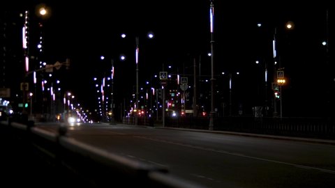 Night traffic on the road, lonely car driving along the street lamps. Stock footage. Night city road with street lights and moving car on dark sky background.
