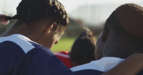 Rear view of a team of young adult multi-ethnic female rugby players standing on a rugby field in a huddle having a moment of silent thought in preparation for a rugby match in slow motion