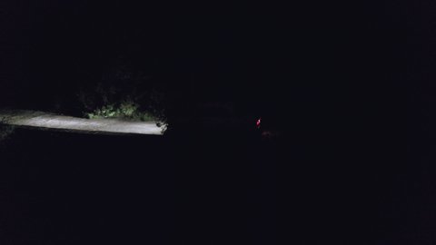 Car moving on countryside road in dark night drone view. Car headlights illuminating night road in darkness. Night car motion aerial view