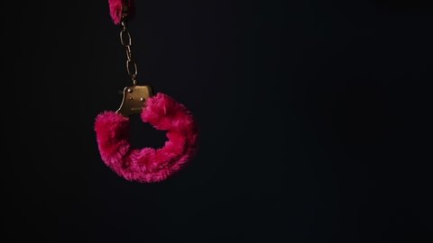 Handcuffs with pink fir on black background. 4K video.