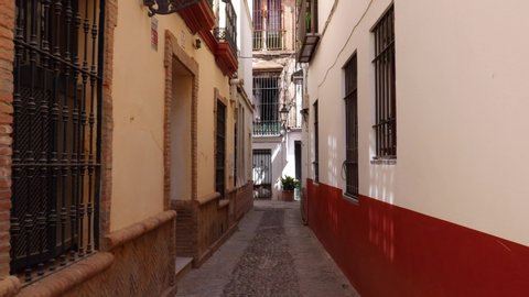 POV walking down old picturesque passageway in the medieval Jewish Quarter of Santa Cruz in Seville, Andalusia, Spain