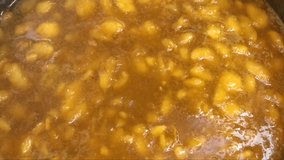 4K hd video of Fresh summer peaches cut up and boiling in sugar and pectin to make fresh homemade peach jam. Close up, hand holding white stirring spoon stirs.