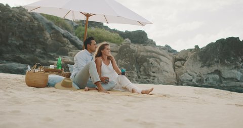 Attractive mixed race couple having a beach picnic, luxurious couple relaxing under a white beach umbrella