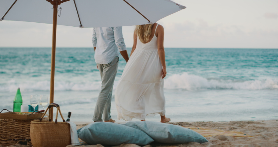 Romantic couple holding hands walking on the beach with a luxurious picnic in the foreground Royalty-Free Stock Footage #1037447201