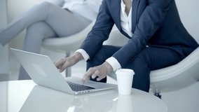 Businesswoman using laptop computer. Close-up partial view of woman in formal wear holding paper cup and typing on laptop in office. Business concept