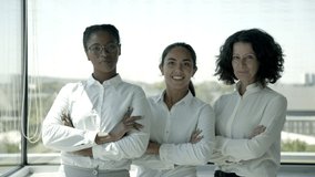 Happy multiethnic businesswomen. Portrait of cheerful multiracial businesswomen in white shirts standing with crossed arms and smiling at camera. Professional team concept