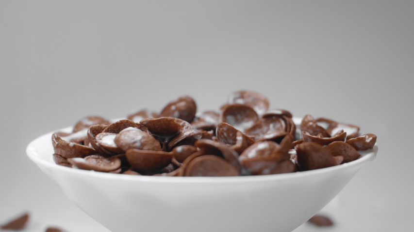 Milk is poured to the bowl with chocolate corn flakes in slow motion, drops of milk falling in 240fps to the cocoa cereal breakfast, liquid in slow motion, Full HD 10 bit uncompressed Royalty-Free Stock Footage #1037450195