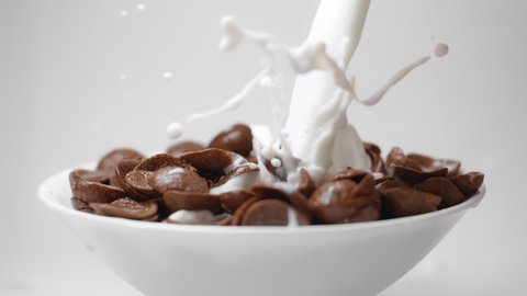 Milk is poured to the bowl with chocolate corn flakes in slow motion, drops of milk falling in 240fps to the cocoa cereal breakfast, liquid in slow motion, Full HD 10 bit uncompressed