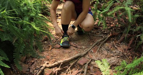 Sportswoman ultramarathon runner tying shoelace in tropical forest 