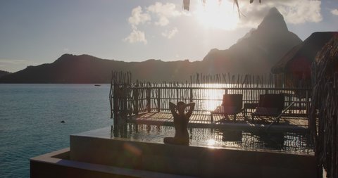 Hotel Luxury resort high end rich people lifestyle woman tourist relaxing watching sunset in infinity pool on private balcony terrace of overwater bungalow suite in Bora Bora, Tahiti, French Polynesia