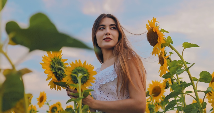 Beautiful girl posing in a field with sunflowers, smiling. Summer landscape with flowers. Camera view from bottom to top.