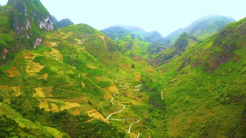 Aerial tilt down of a winding road cut into the mountainside of the misty mountains of Ma Pi Leng Pass in northern Vietnam.
