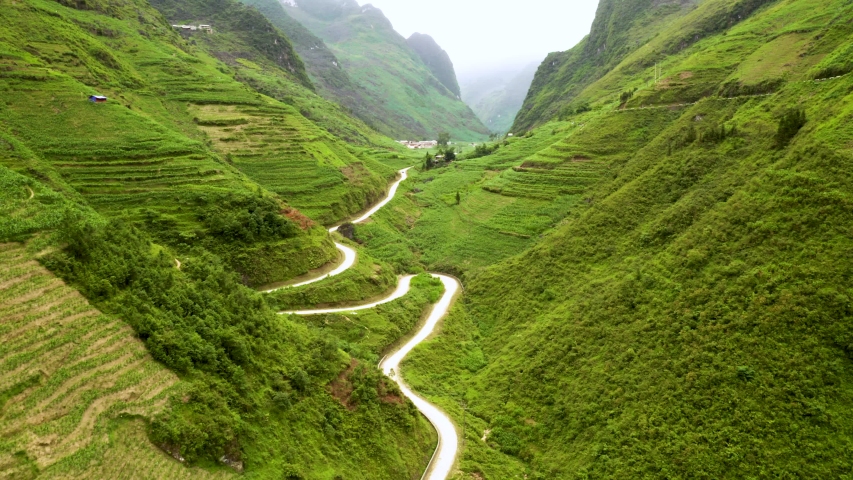 Beautiful winding road carved into a gorgeous lush green valley in Ma Pi Leng pass in northern Vietnam. Aerial Dolly up while tilting down.