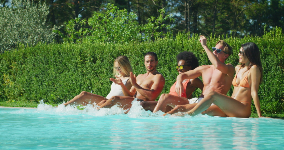 Slow motion of young multi-ethnic friends in swimwear are having fun to enjoy their summer vacation together in swimming pool and playing with a water in a sunny day.