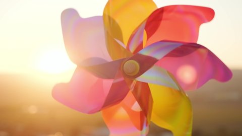 Pinwheel rotate color plastic, windmill with blowing wind meadow of tall grass in mountains on sunny day at sunset in autumn blue sky. Descending bright disk of sun beyond horizon. Relax