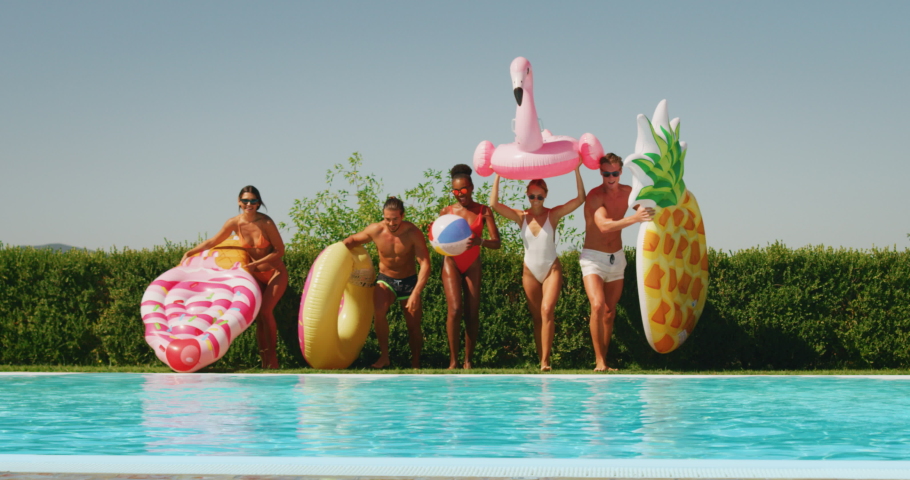 Slow motion of young multi-ethnic friends in swimwear are having fun to enjoy their summer vacation together and jumping in a water  with colorful inflatables in a sunny day. Royalty-Free Stock Footage #1037471186