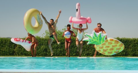 Slow motion of young multi-ethnic friends in swimwear are having fun to enjoy their summer vacation together and jumping in a water  with colorful inflatables in a sunny day.
