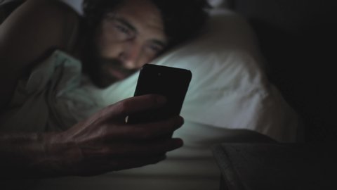 A man sleeping in a bed woken by phone call on a smart phone 4K