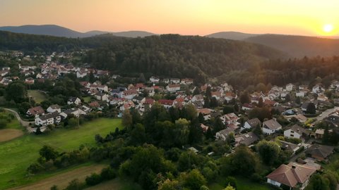 Village surrounded by beautiful hilly green landscape at a colorful sunrise, aerial footage
