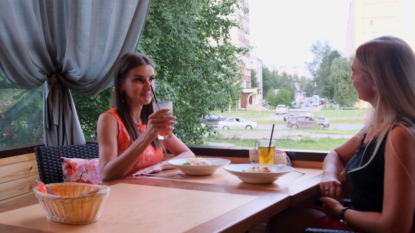 Two friends in a cafe-bar drink cocktails on an open terrace