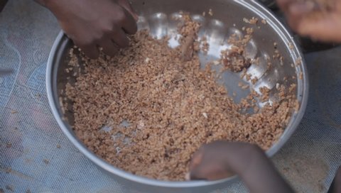 Sambouya, the Gambia, Africa, October 22, 2018: close up of a silver bowl full of brown rice, and kids hands reaching for it, outdoors on a sunny day